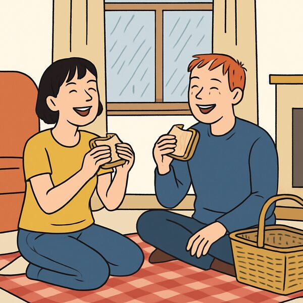 The woman and the man sit on the blanket on the living room floor, eating the picnic and laughing, with rain on the window.