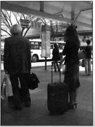 Two travellers with luggage waiting under a canopy at a bus stop